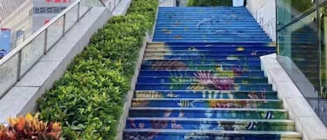 A staircase with a colorful mural, surrounded by greenery and modern buildings.