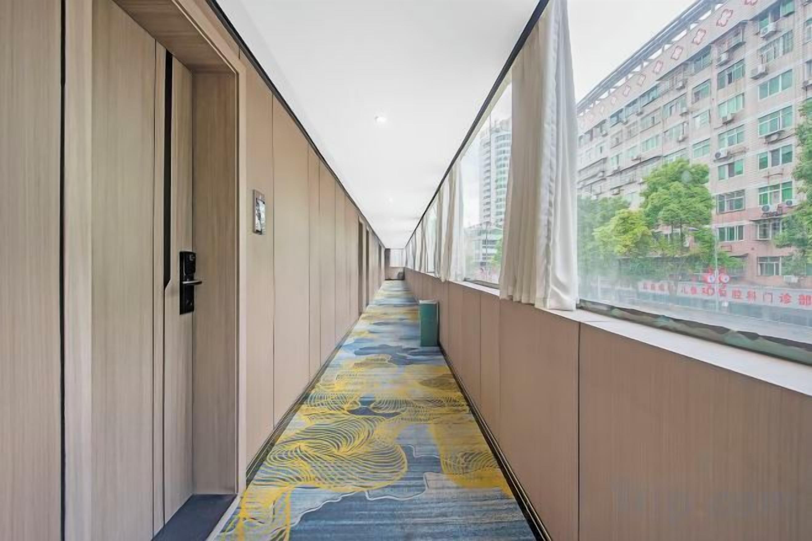 Un couloir avec un tapis à motifs, des murs en bois et une fenêtre donnant sur des immeubles.