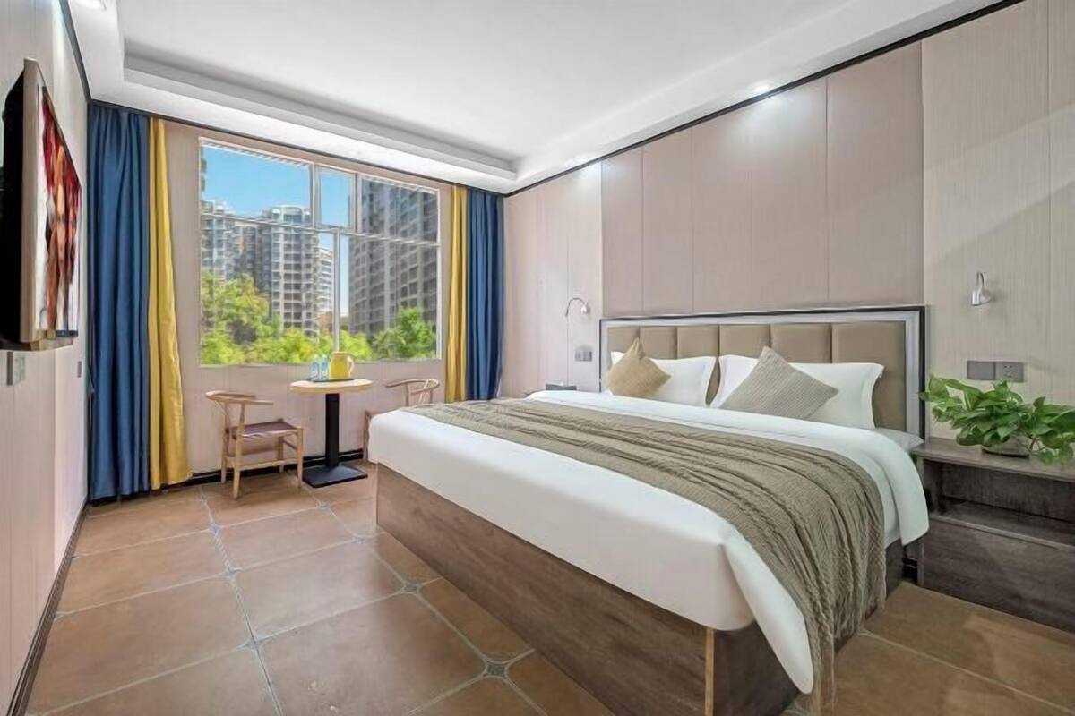 Une chambre d’hôtel avec un grand lit, une télévision, une petite table et une vue sur les immeubles par la fenêtre.