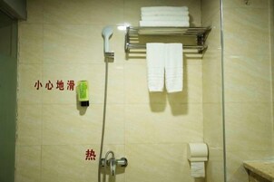 Un baño con ducha, un perchero con toallas y un dispensador de jabón.