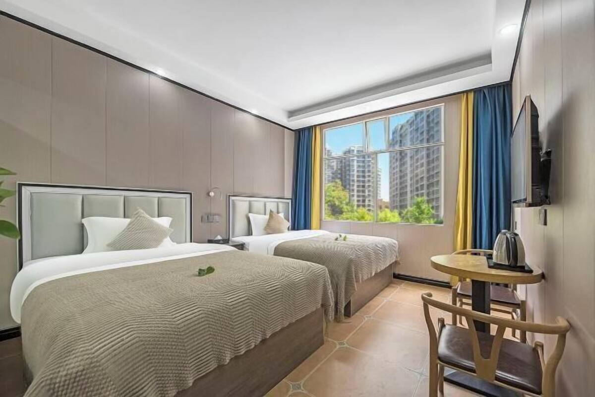 Une chambre d’hôtel avec deux lits, une petite table et une fenêtre avec des rideaux.