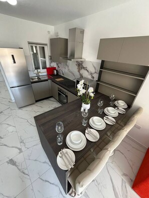 A modern kitchen with a marble backsplash, stainless steel appliances, and a dining area set for six with white plates and glasses. - NEW Sea-side Hot Tub Lux Apartment (Saint Pauls Bay)