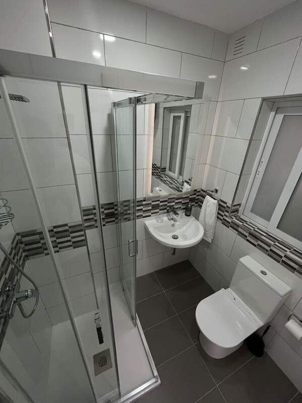 A modern bathroom with a glass shower enclosure, a white sink, and a toilet.