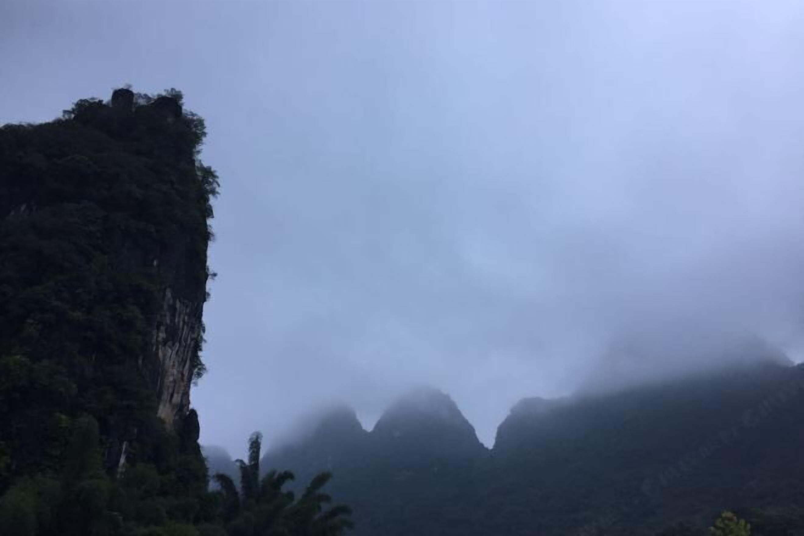Un paisaje montañoso con vegetación densa y un acantilado prominente.