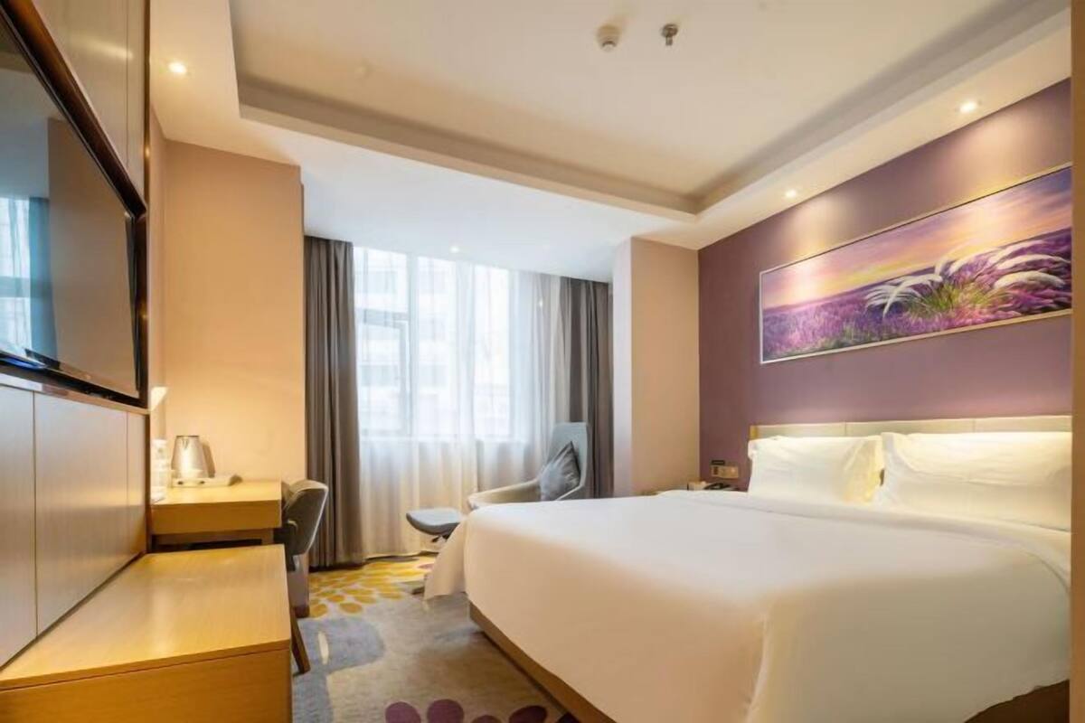 Hotellihuone, jossa on sänky, työpöytä, tuoli, televisio ja taulu seinällä.