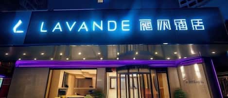 A hotel entrance with a neon sign, a glass door, and a small outdoor seating area.