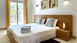 Ein Doppelbett mit Holz-Kopfstück, zwei Nachttische mit Lampen und Blick auf einen Balkon mit gelben Vorhängen.
