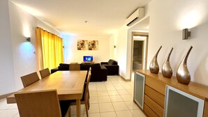Ein modernes Wohnzimmer mit einem Holzes Esstisch, einer Couch und einem Fernseher.