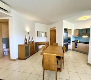 A modern kitchen with a dining area, featuring a large wooden table, built-in appliances, and a tiled floor. - Paradise in Santa Maria (Sal)
