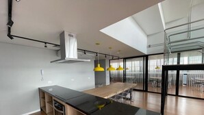 A modern kitchen with a black countertop, wooden cabinets, and a built-in oven. There are yellow pendant lights and a large dining table with chairs. - Decorated 2 bedroom apartment in the center (Centro Curitiba)
