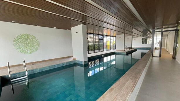 A long indoor swimming pool with clear water, wooden ceiling panels, and a large window providing natural light. - Decorated 2 bedroom apartment in the center (Centro Curitiba)