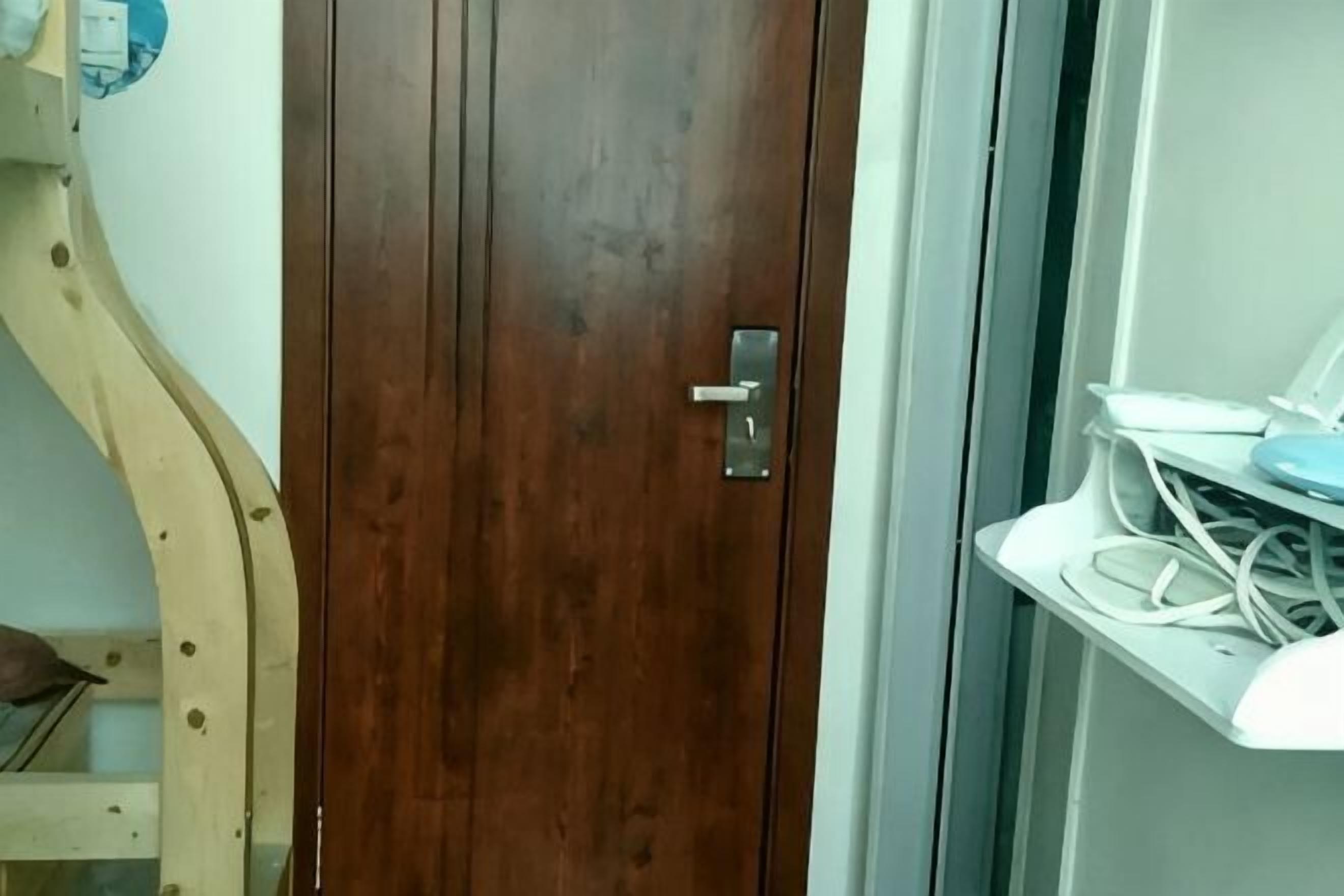 Eine Holztür mit Griff, ein weißes Regal mit Gegenständen und ein Teil eines Bettgestells.