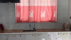 A kitchen with a sink, a window with a pink curtain, and a microwave. - Kailai Hotel (Mohe)