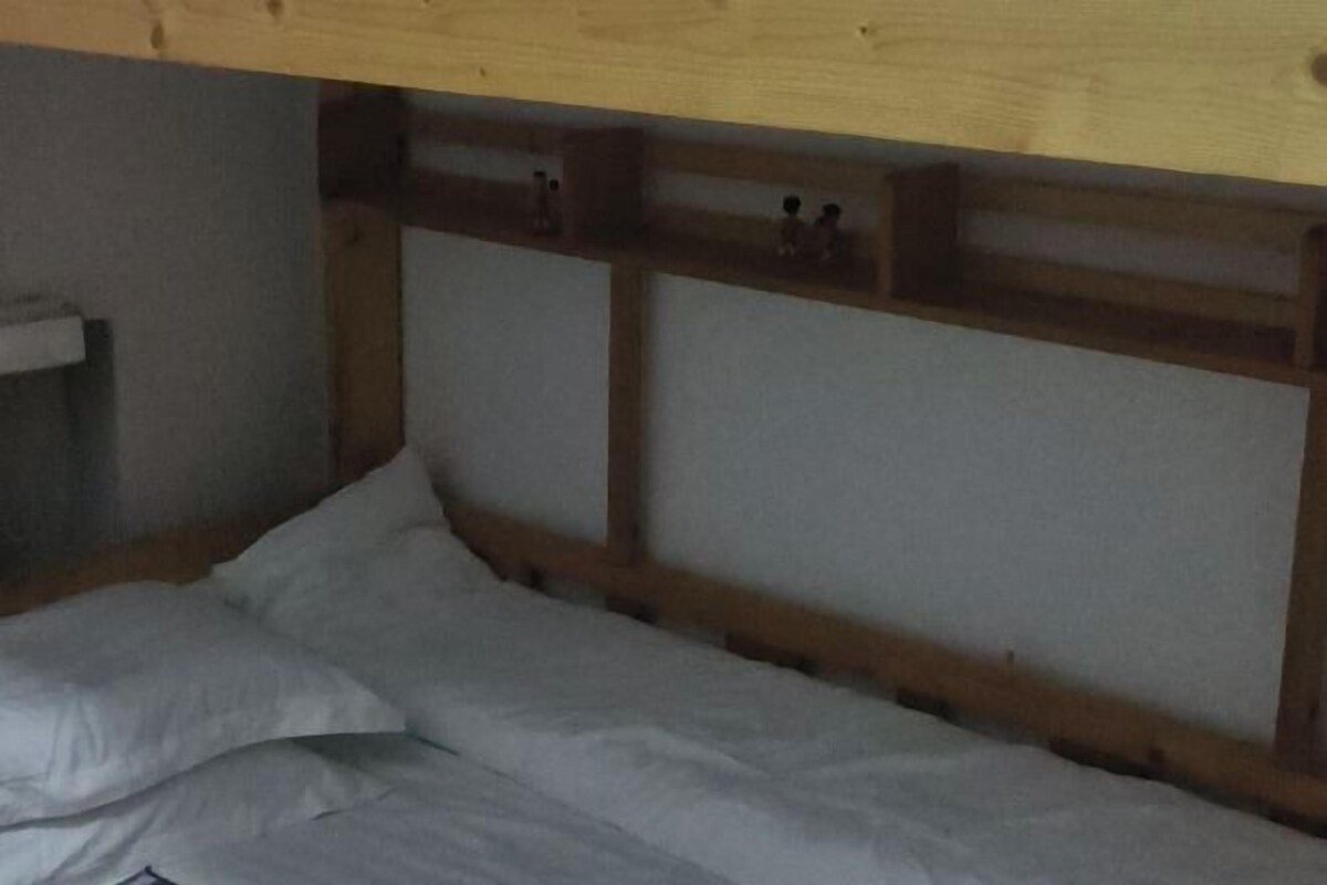 A wooden headboard with a simple design, a white pillow, and a small shelf with items on it.