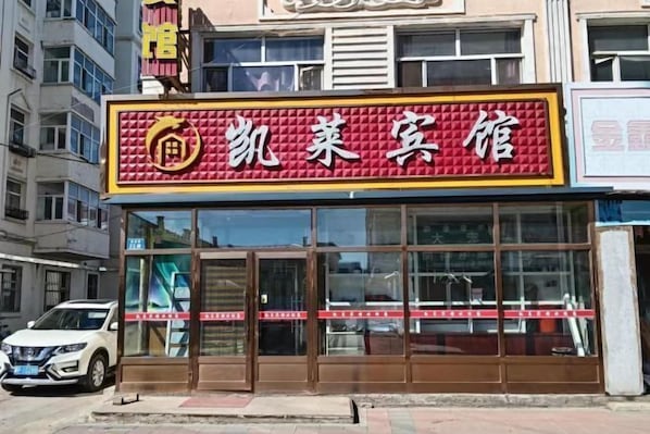 A hotel with a red and yellow signboard, large glass windows, and a white car parked in front. - Kailai Hotel (Mohe)