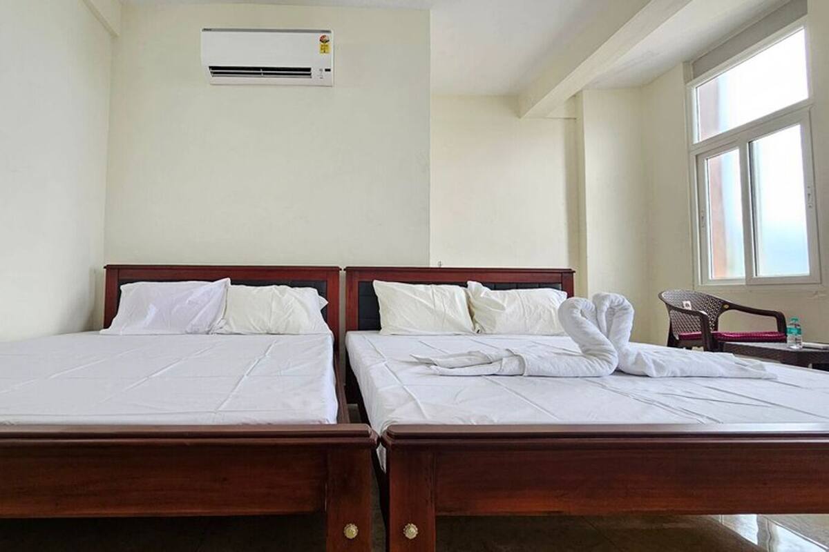 A hotel room with two beds, a window, and an air conditioning unit.