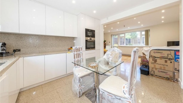 A modern kitchen with white cabinets, a granite countertop, and a glass table. There are boxes and a vacuum cleaner in the room. - Beaconsfield (Luton)