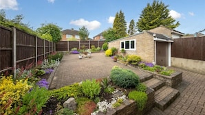 A backyard with a brick patio, potted plants, and a small brick structure. - Beaconsfield (Luton)