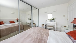 A hotel room with a large bed, a desk, a mirror, and a fireplace. - Beaconsfield (Luton)