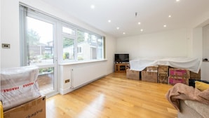 A spacious living room with large windows, a flat-screen TV, and boxes indicating recent moving activity. - Beaconsfield (Luton)