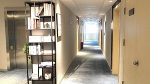 A hallway with a bookshelf, a door, and a view into another room. - Magnotel Hotel (Nanchang Bayi Square People's Park Metro Station) (Nanchang)