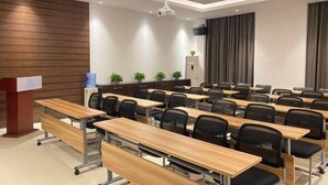 A conference room with multiple rows of desks and chairs, a podium, and a projector. - Magnotel Hotel (Nanchang Bayi Square People's Park Metro Station) (Nanchang)