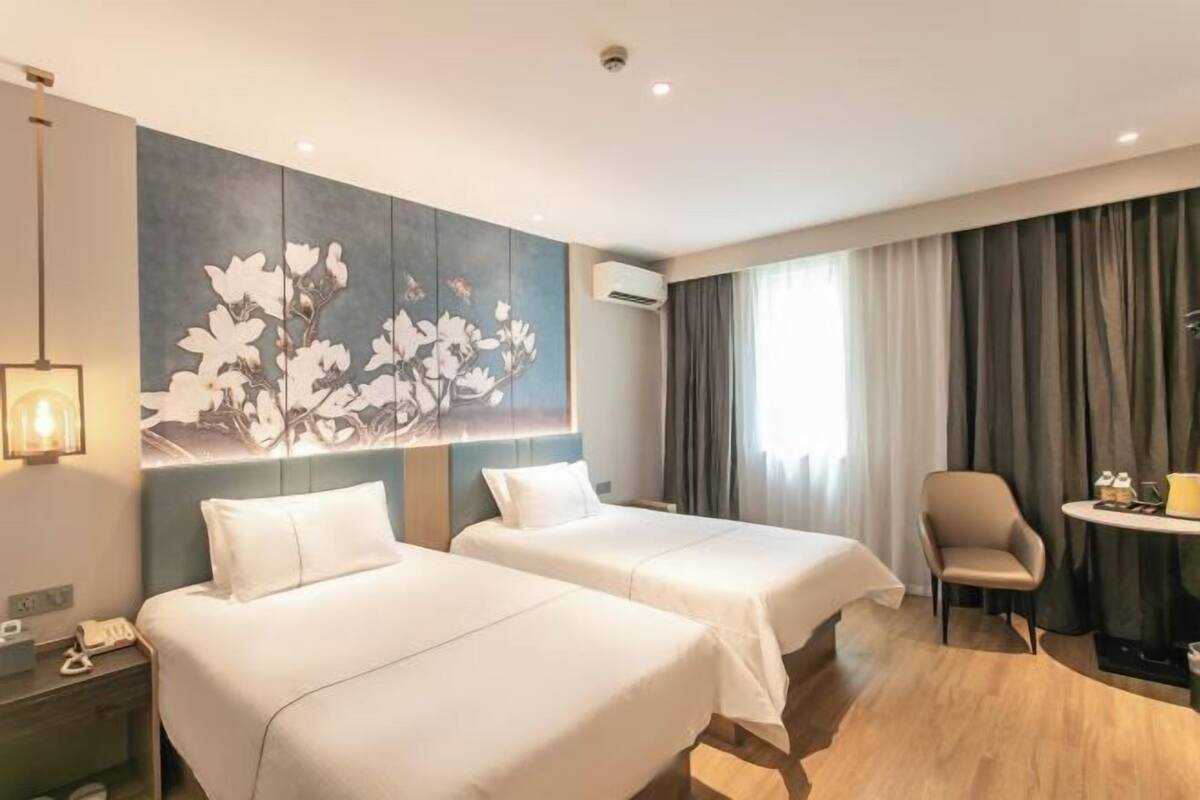 Una habitación de hotel con dos camas, un escritorio, una silla y una gran obra de arte floral en la pared.
