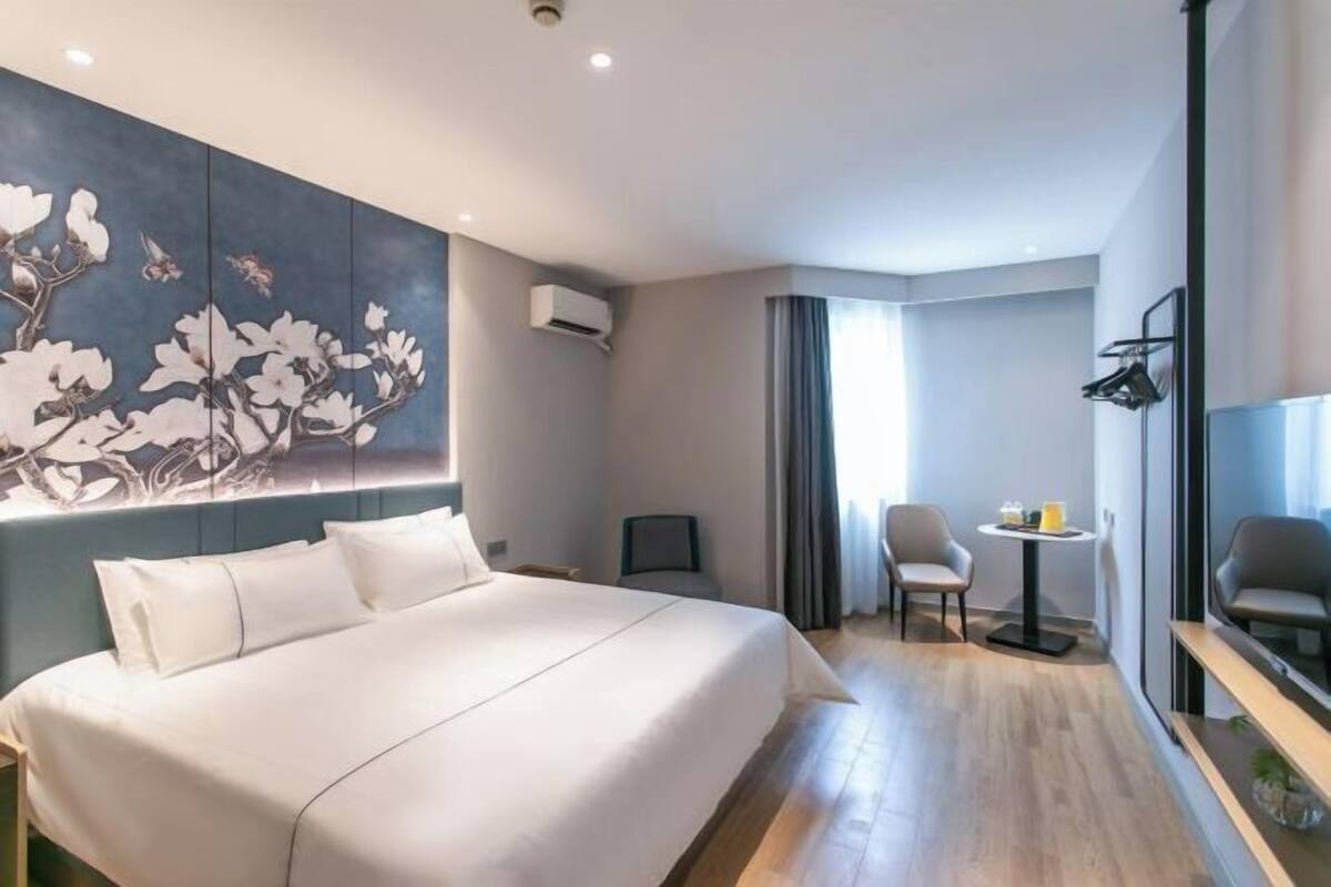 Habitación de hotel con una cama grande, un escritorio con silla, una mesita con otra silla y un cuadro grande en la pared.