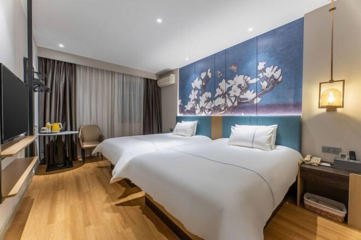 Habitación de hotel con dos camas, un televisor de pantalla plana, un escritorio con silla, un cuadro en la pared y una mesita de noche con lámpara.