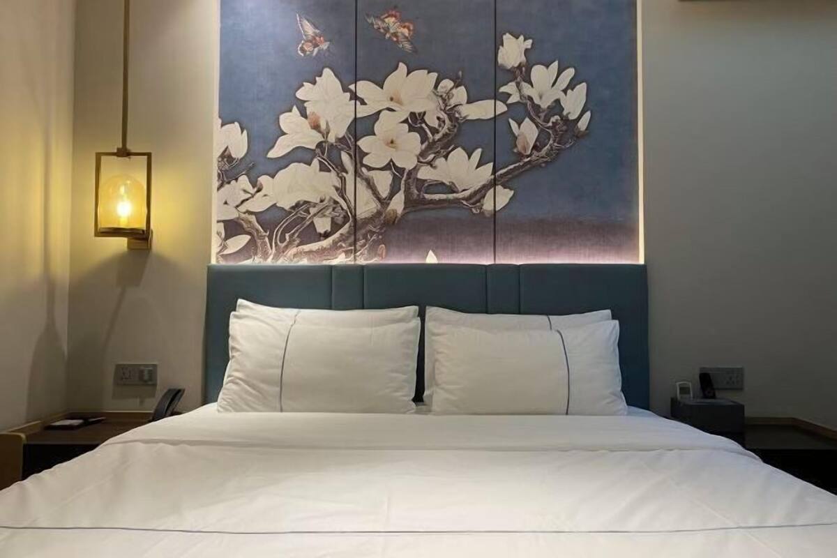 Una habitación de hotel con una cama, una lámpara fijada a la pared y un cuadro decorativo.