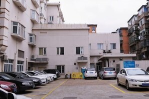A parking lot with multiple cars, a building with balconies, and a sign on the right. - Magnotel Hotel (Nanchang Bayi Square People's Park Metro Station) (Nanchang)