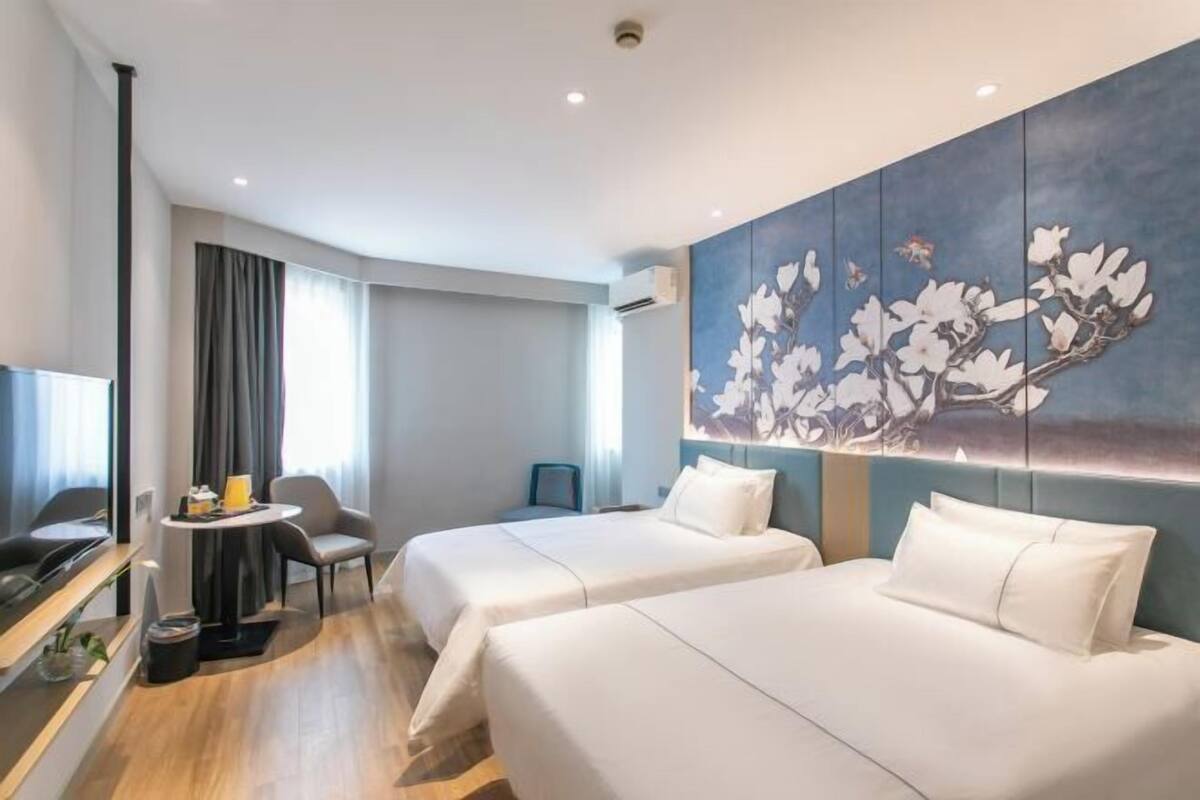 Habitación de hotel con dos camas, una mesa de comedor, un televisor y una gran obra de arte floral en la pared.