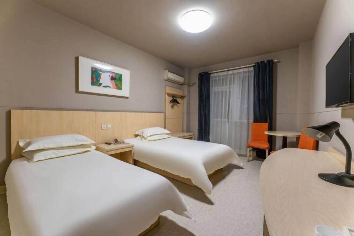 Habitación de hotel con dos camas, un escritorio, una silla, un televisor y un cuadro en la pared.