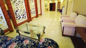 A hotel lobby with a glass coffee table, patterned sofas, and decorative screens. - Tian Zuan Wang Chao Hotel (Huai'an)