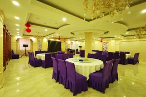 Un salón de banquetes con mesas redondas y sillas moradas, un escenario y una araña.