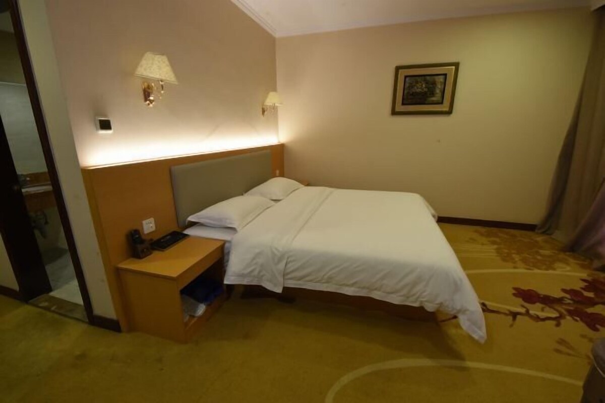 Habitación de hotel con cama, mesita de noche, lámpara y un cuadro en la pared.