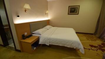 A hotel room with a bed, bedside table, lamp, and a painting on the wall.