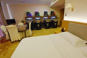 Una habitación de hotel con cama, escritorio con computadora y cuatro sillas con visores iluminados.