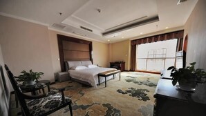 A hotel room with a bed, a desk, a chair, a small table, and a potted plant. - Tian Zuan Wang Chao Hotel (Huai'an)