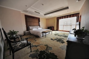 A hotel room with a bed, a desk, a chair, a small table, and a potted plant. - Tian Zuan Wang Chao Hotel (Huai'an)