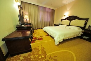 Una habitación de hotel con cama, escritorio, lámpara, mesita de noche y ventana con cortinas.