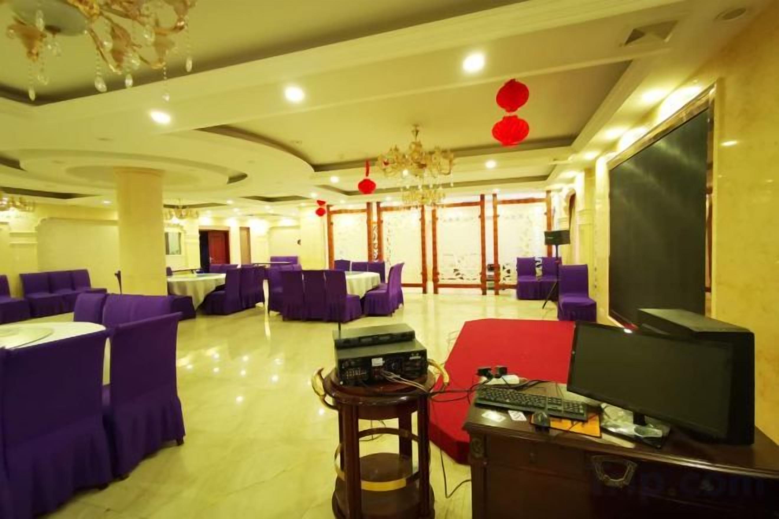 Un hall d’hôtel avec des sièges violets, un canapé rouge, un téléviseur et un ordinateur posé sur un bureau.