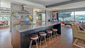 Una cocina moderna con una isla central, taburetes de bar y un amplio ventanal con vistas al exterior.