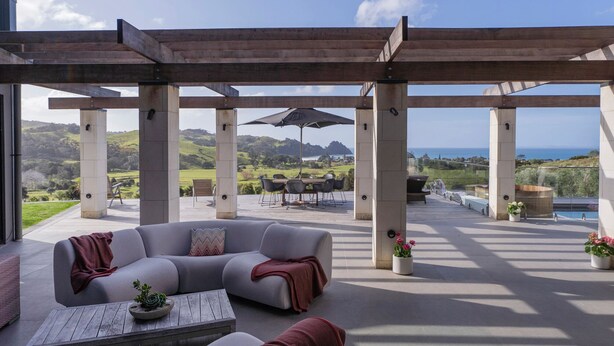 Un patio exterior con un sofá gris, una mesa de madera y una pérgola.
