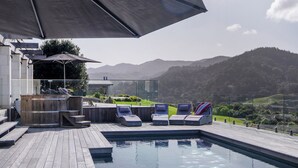 Un área junto a la piscina con sillones reclinables, un jacuzzi y una terraza de madera.