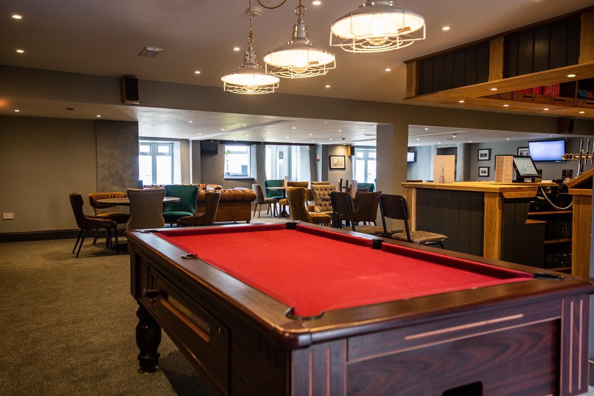 A pool table in a room with multiple seating areas, a bar, and large windows.