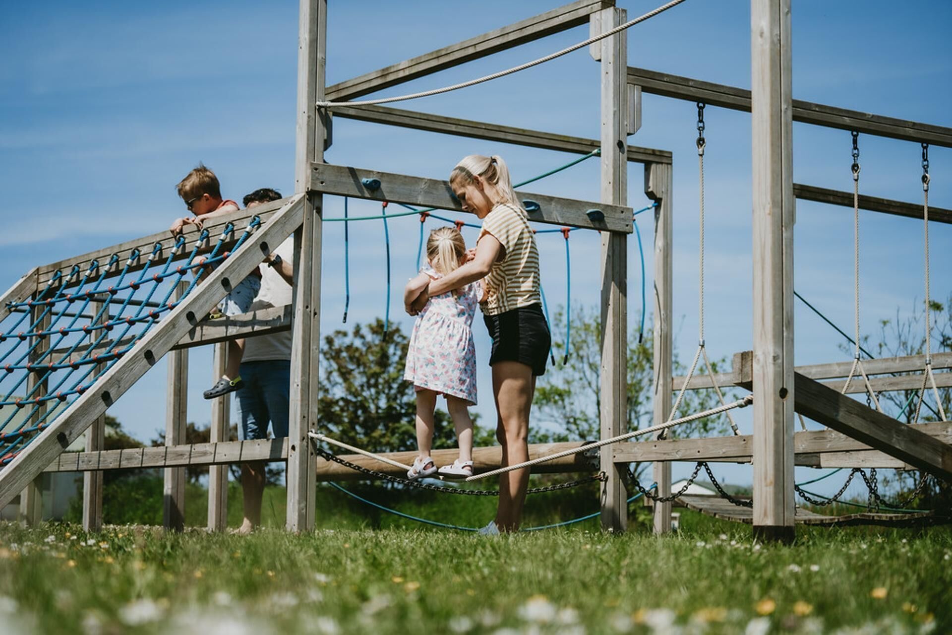 A wooden playground structure with a rope bridge and a netted climbing area.