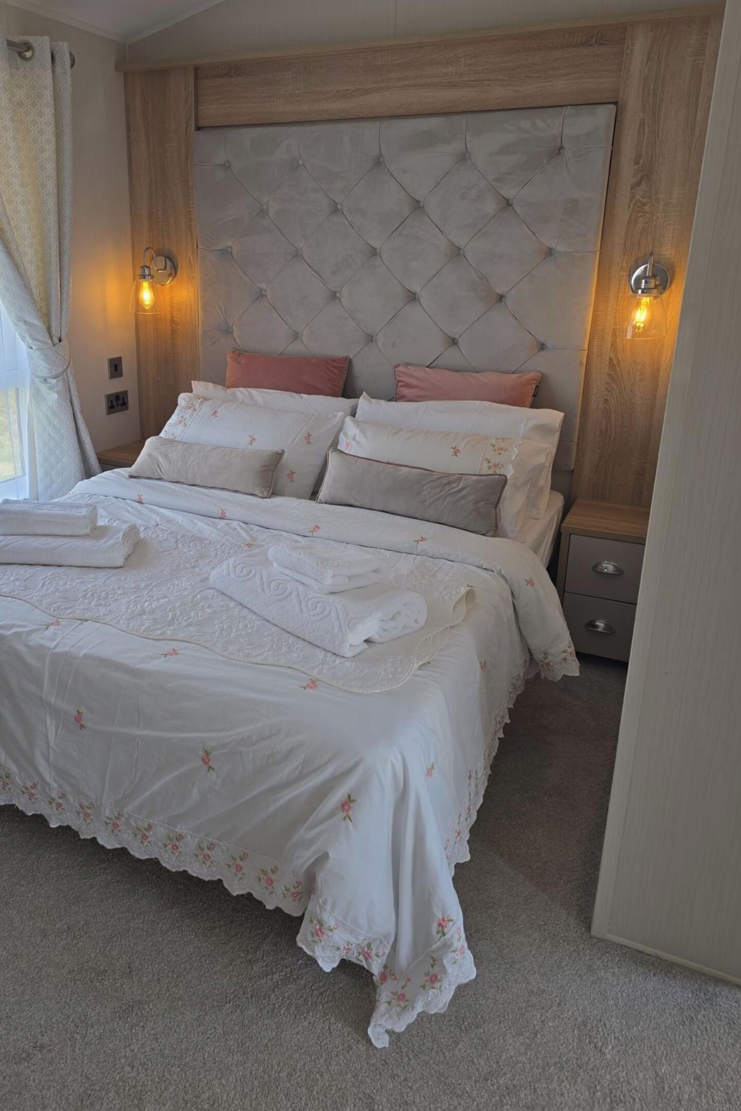 A neatly made bed with a tufted headboard, a bedside table with a lamp, and a carpeted floor.