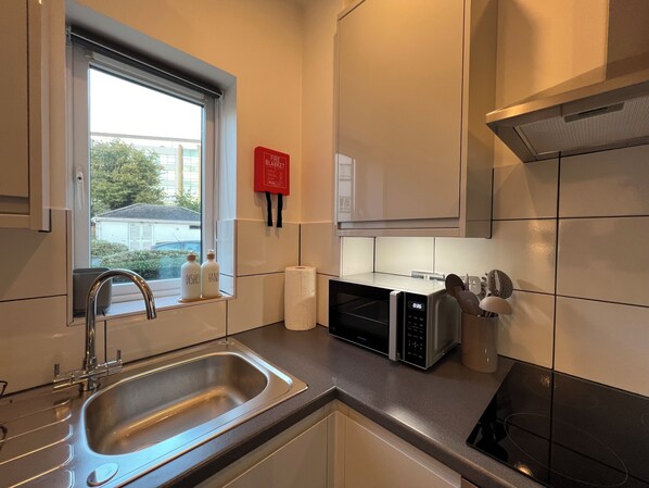 A modern kitchen with a stainless steel sink, a microwave, a toaster, and a window with a view of the outside. - Modern apartment in the vicinity of Heathrow/Windsor/Slough (Slough)