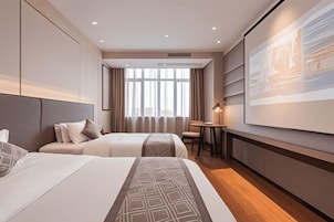 Habitación de hotel con dos camas, un escritorio, una silla y un amplio ventanal con cortinas.